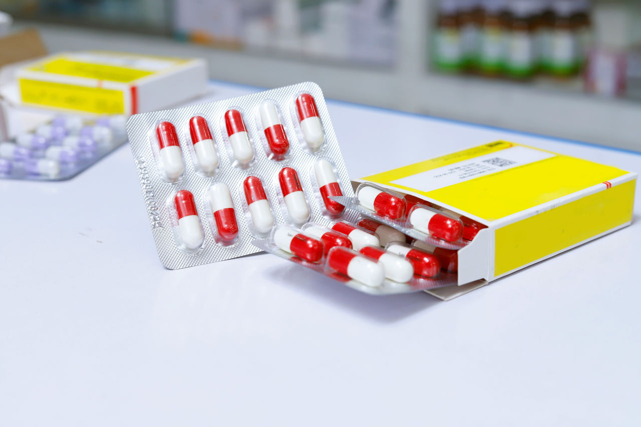 Blisterpackungen mit rot-weißen Kapseln, teilweise aus einer gelb etikettierten Packung entnommen.