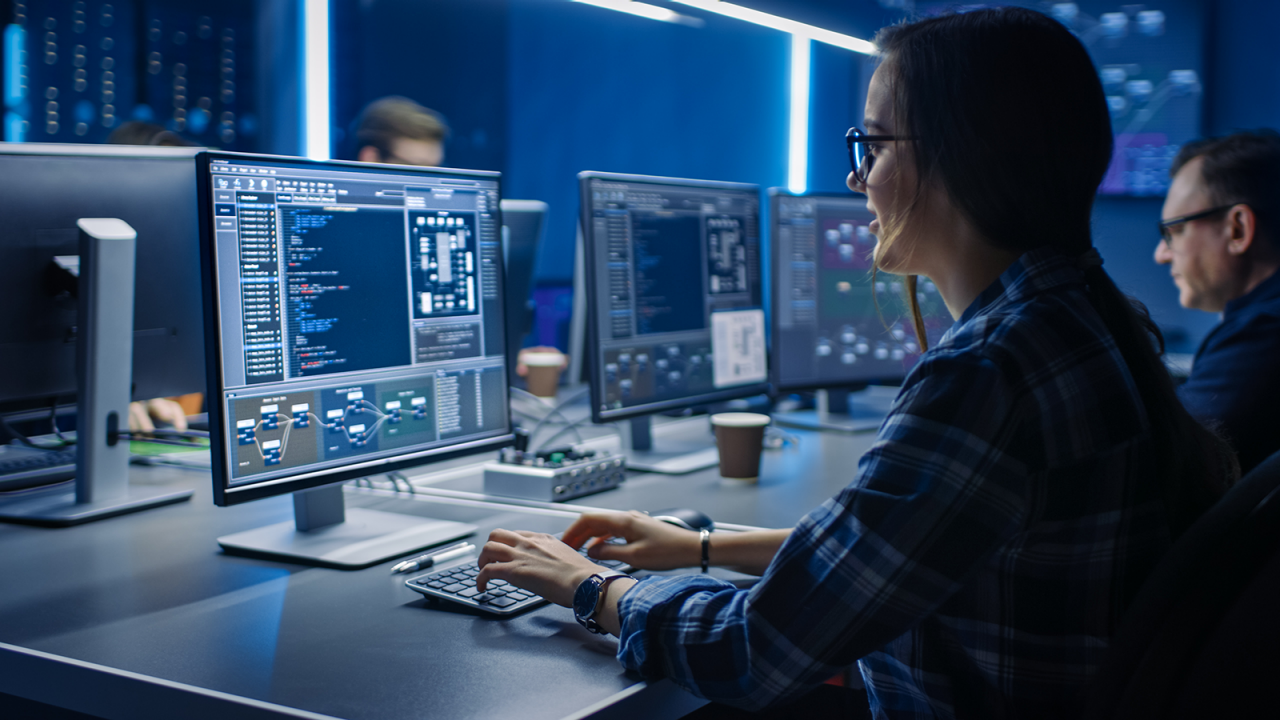 Female programmer coding innovative processes on a desktop as part of a team.