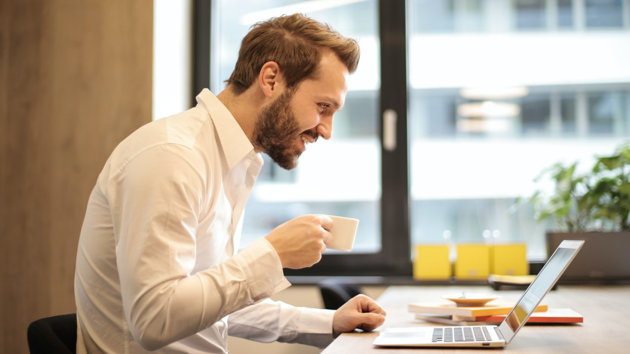 A young marketing professional carrying out A/B testing using Minitab while smiling and holding a cup of coffee.