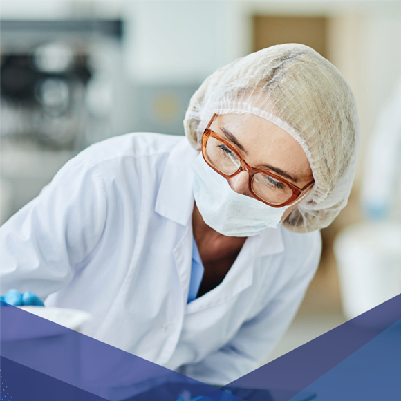 Técnico de laboratorio con cubrebocas, cofia y lentes, trabajando en un entorno clínico o estéril.