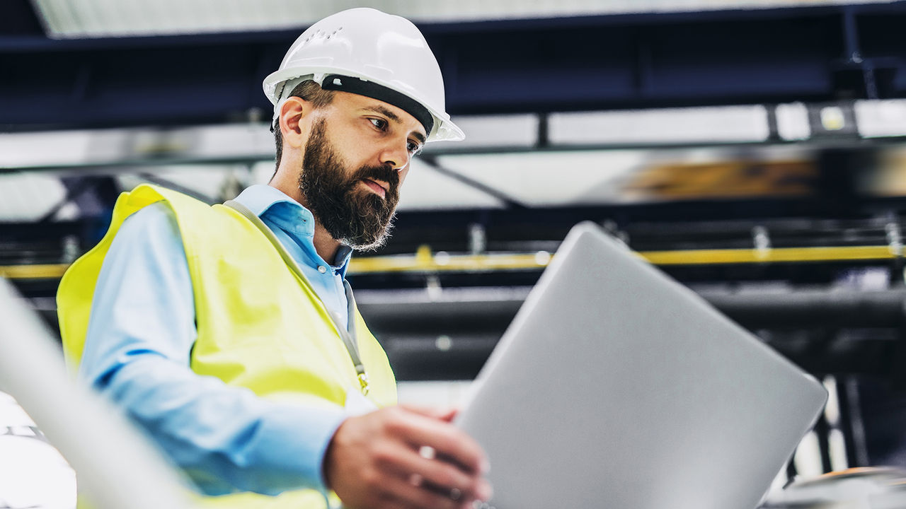 A portrait of an industrial man engineer with laptop in a factory, working. A portrait of an industrial man engineer with laptop in a factory, working.